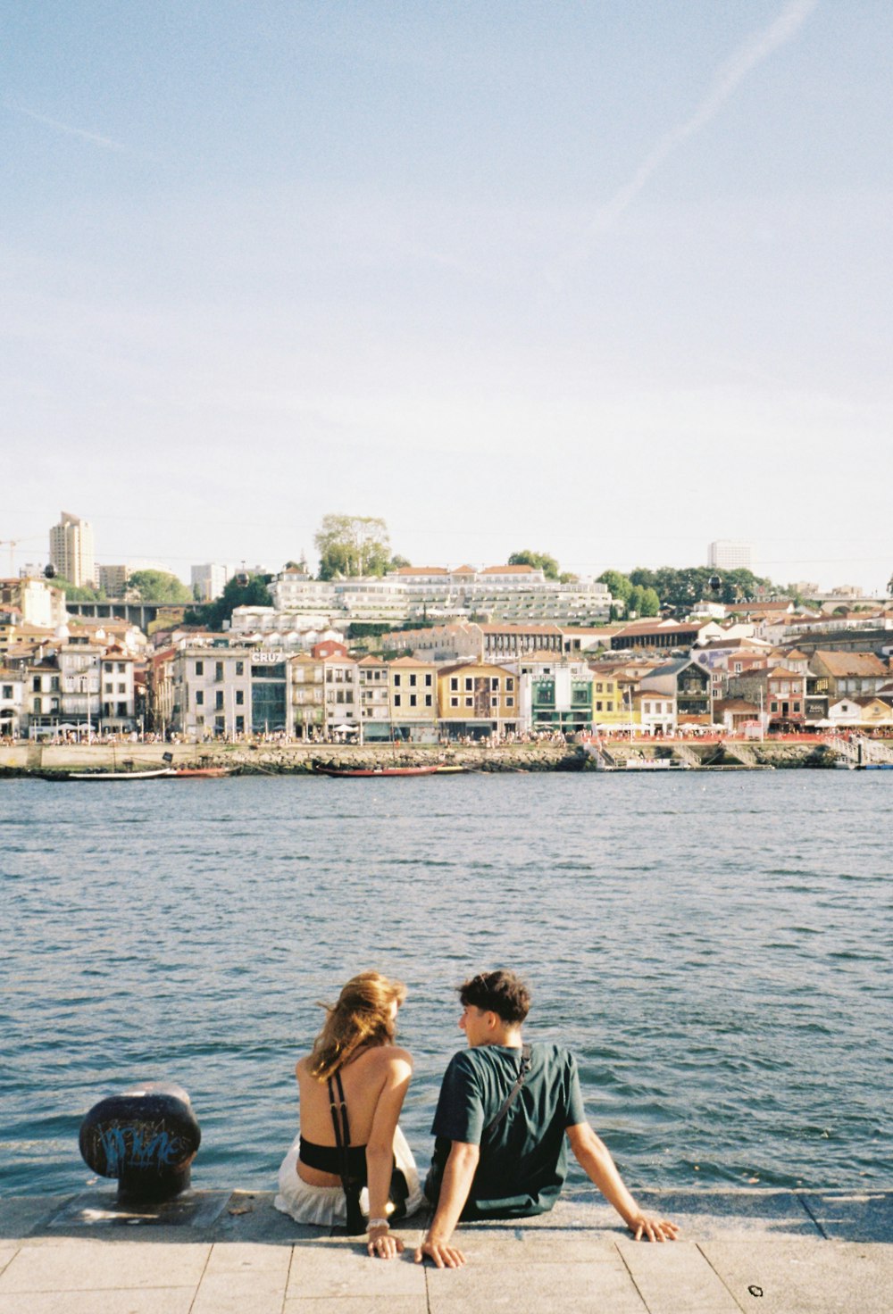 a man and a woman sitting on a dock next to a body of water