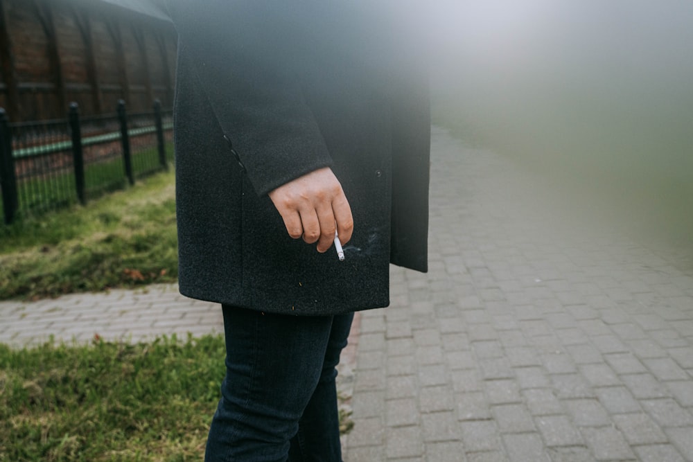 uma pessoa em pé em uma calçada com um cigarro na mão