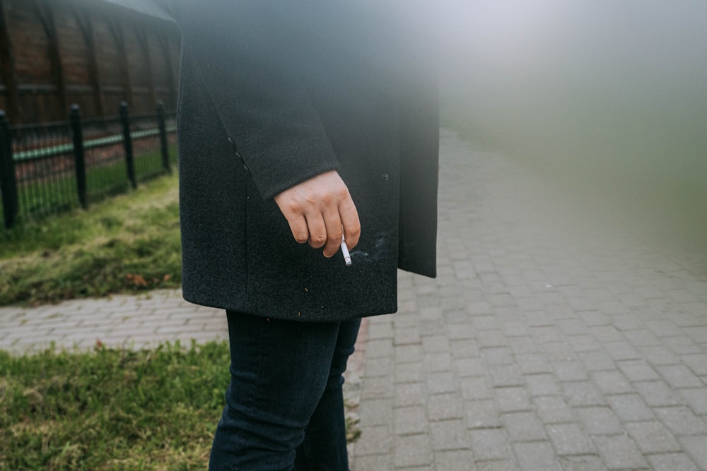 a person standing on a sidewalk with a cigarette in their hand