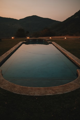 an empty swimming pool in a field with mountains in the background