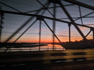 the sun is setting over the water from a bridge