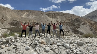 A diverse group of people holding hands in a circle on open land under a clear sky.