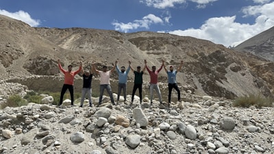A diverse group of people holding hands in a circle on open land under a clear sky.