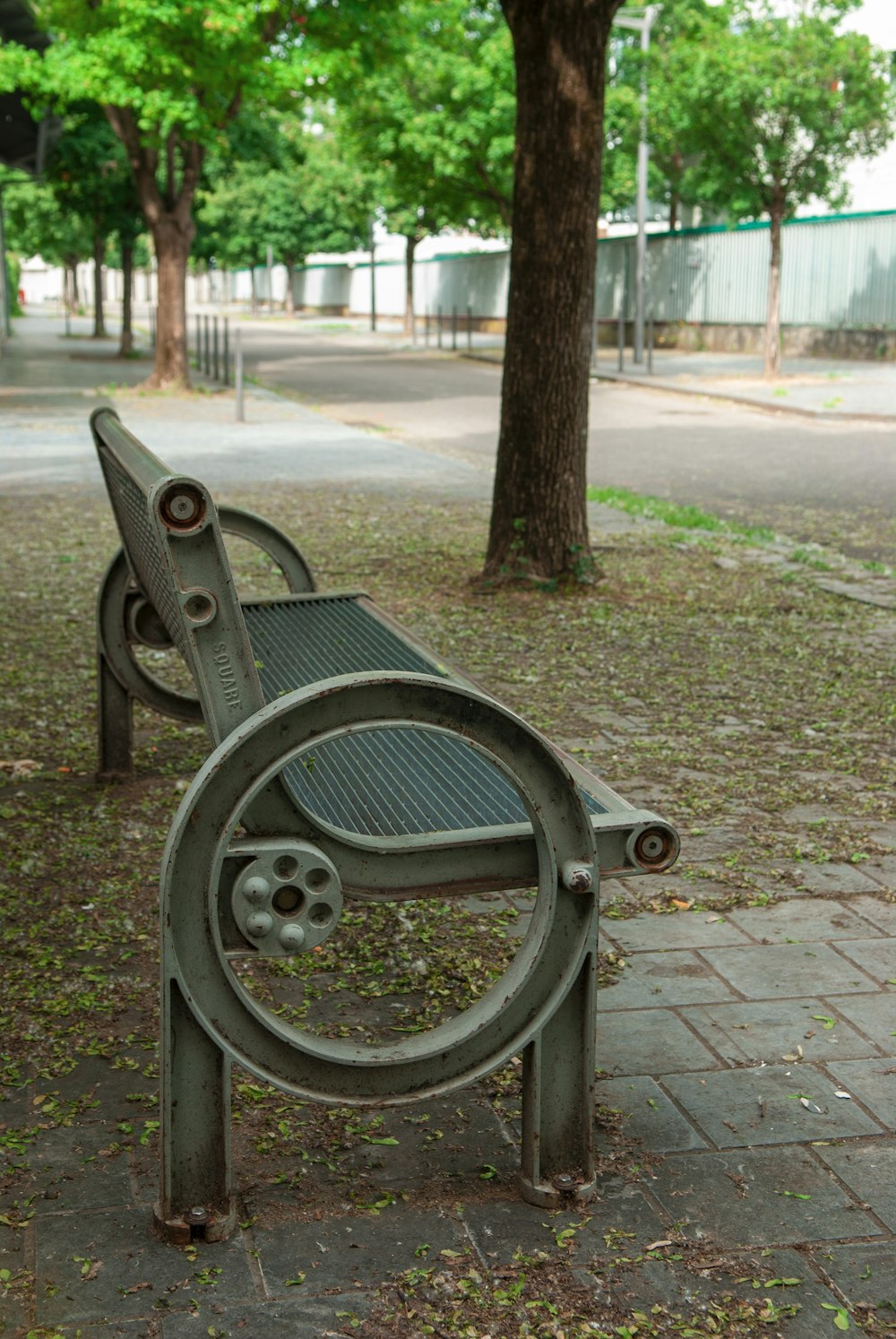 a metal bench sitting on top of a sidewalk next to a tree