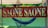 A rust-colored metal sign with cut-out letters spelling 'SAONE SAONE' is prominently displayed. Behind the sign, a blue hammock hangs between poles with a decorative lantern above. In the background, a lush, green landscape and a calm body of water are visible.