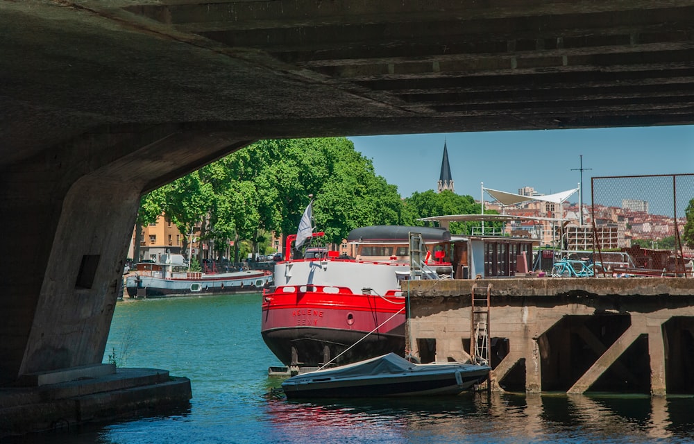 a red and white boat in the water under a bridge