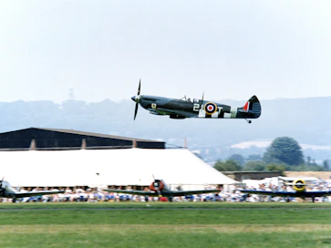 Historic RAF Spitfire flying over a wartime airfield at dawn.