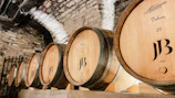 A cinematic close-up of oak barrels aging fine wine in a dimly lit cellar.