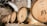 Wooden wine barrels are lined up against a stone wall in a dimly lit cellar. The barrels have logos and inscriptions on them, indicating a winery setting.