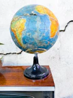 A rustic antique globe with faded maps sitting on a wooden desk by a window.