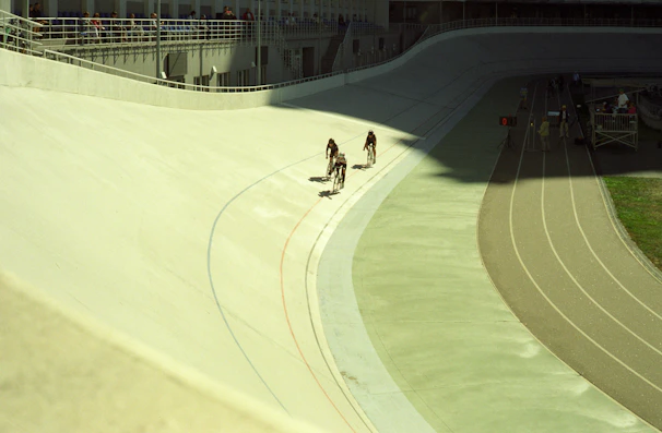 A high-energy cycling race underway on a sunlit, winding track surrounded by cheering spectators.