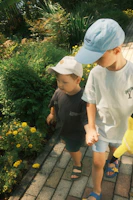 Children smiling and holding hands in a sunny outdoor garden filled with sunflowers.