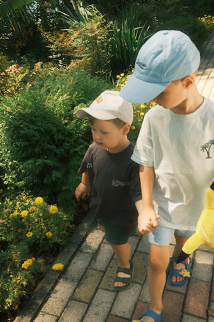 Children barefoot, holding hands, walking slowly through a sun-dappled meadow filled with wildflowers.