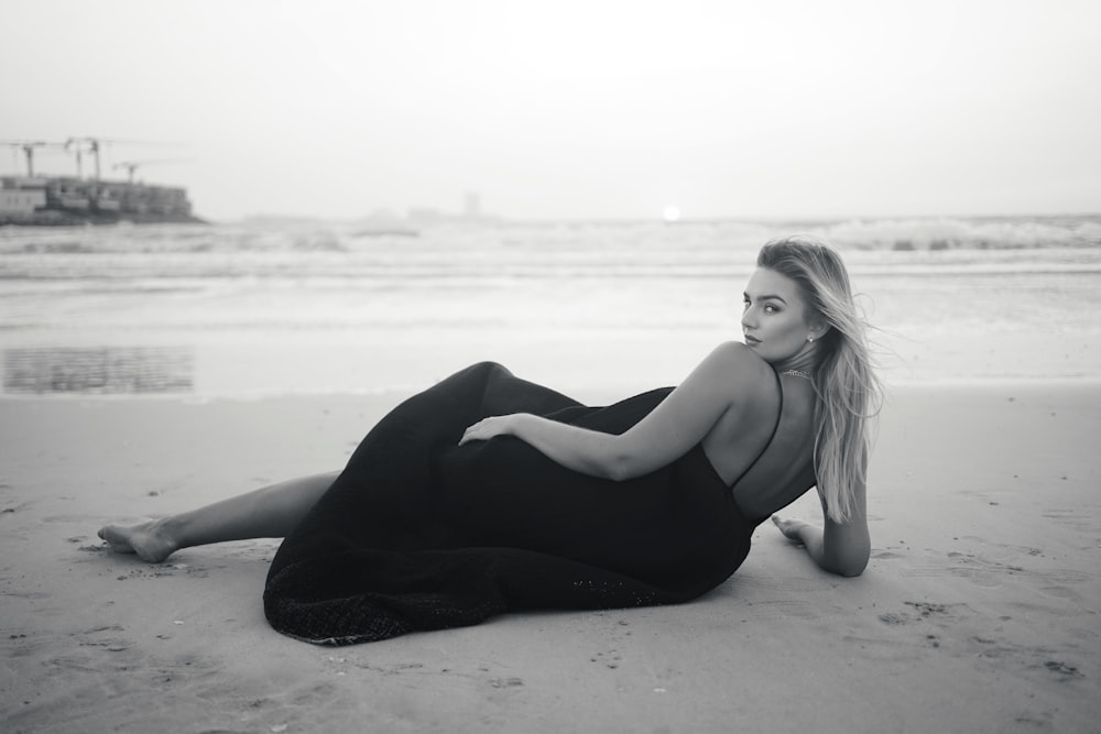 a woman sitting on the beach in a black dress