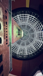 A tall brick building extends upward, surrounded by a large, intricate glass and steel cone structure. The words 'R.M. Williams' are visible on the side of the building. The architectural design suggests a blend of historical and modern elements.