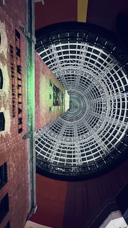 A tall brick building extends upward, surrounded by a large, intricate glass and steel cone structure. The words 'R.M. Williams' are visible on the side of the building. The architectural design suggests a blend of historical and modern elements.