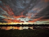 A vibrant river scene at sunset with boats drifting near lush green banks.