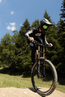 Mountain biker navigating a rugged trail surrounded by pine trees under a bright blue sky.