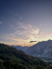 A panoramic view of two lush green hills under a vibrant orange sunrise gradient.