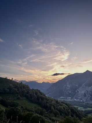 A panoramic view of two lush green hills under a vibrant orange sunrise gradient.