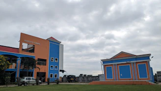 A warm, sunlit photo of Saraswati Sishu Vidya Mandir’s main building framed by deep saffron and royal blue banners.