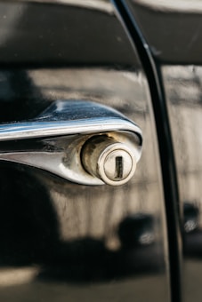 A close-up view of a vintage car door handle with a classic keyhole, featuring a metallic and slightly worn appearance.