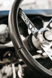 Close-up of a vintage Formula 1 steering wheel with worn leather grips and polished metal spokes, set against a dark racing cockpit background.