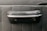A close-up view of a textured black material featuring a protruding handle-like object, possibly part of a vehicle's interior door panel. The handle has a smooth, polished metallic trim and a black leather-like covering.