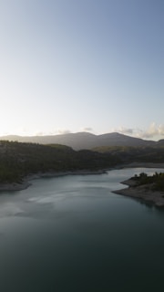 A serene landscape featuring a calm lake surrounded by lush greenery and distant mountains under a clear blue sky.