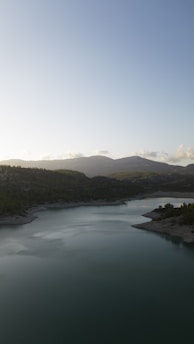 A serene landscape featuring a calm lake surrounded by lush greenery and distant mountains under a clear blue sky.