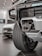 Close-up view of a rugged vehicle's front section in a showroom, focusing on the grille, tire, and towing hitch. The background features another car with visible details in a well-lit environment.