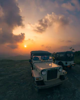 Two buggys parked on a hilltop overlooking a vast mountain landscape at sunset
