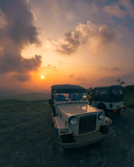 Two buggys parked on a hilltop overlooking a vast mountain landscape at sunset