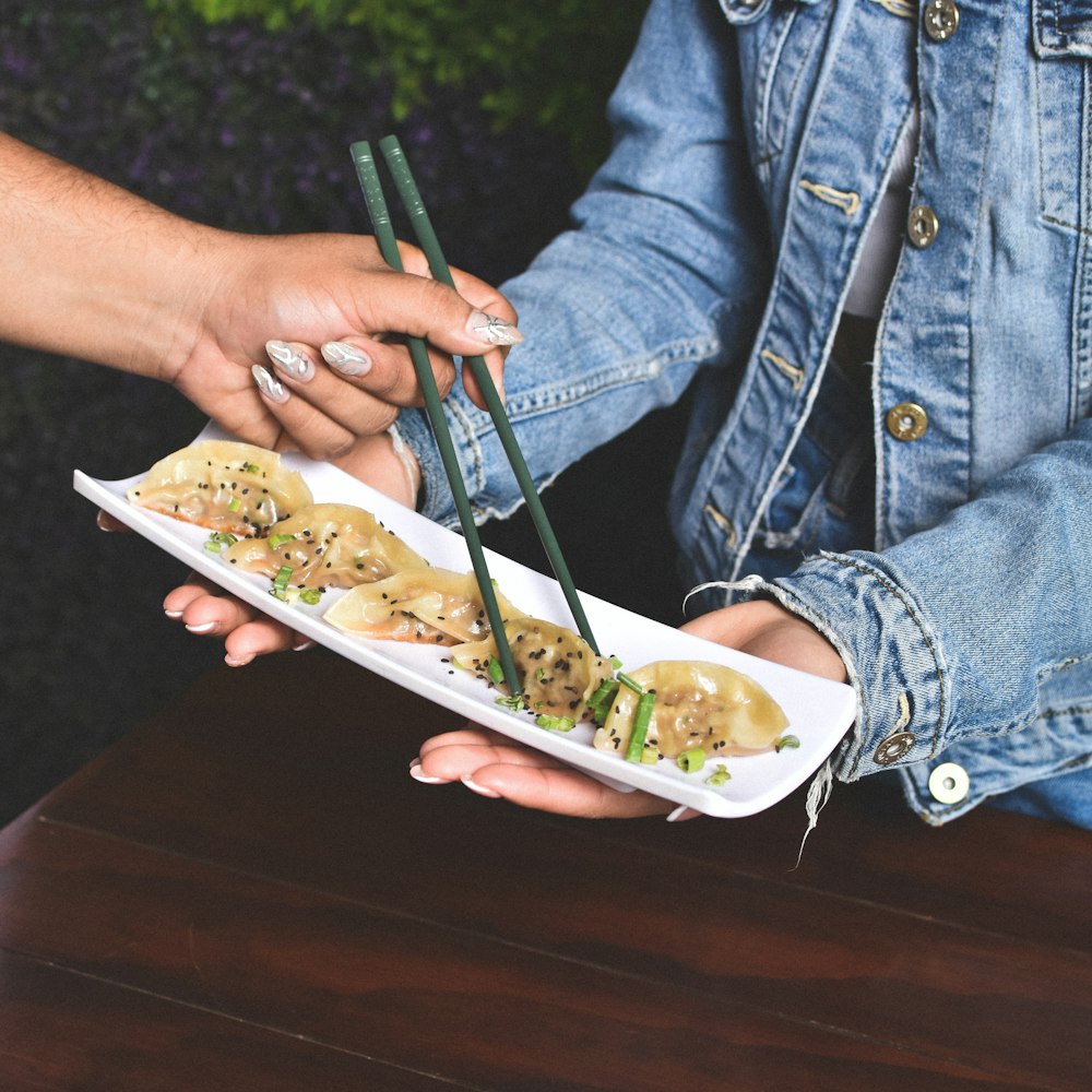 a person holding a plate of food with chopsticks