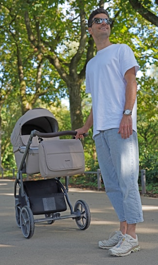 A happy parent folding a compact stroller with their smiling baby inside, outdoors on a sunny day.