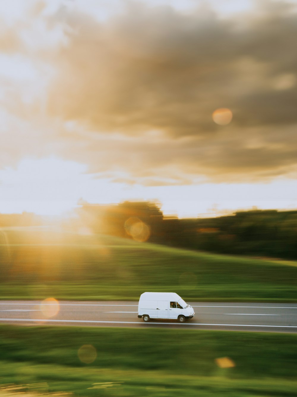 Ein weißer Lieferwagen, der eine Straße neben einem üppig grünen Feld entlangfährt