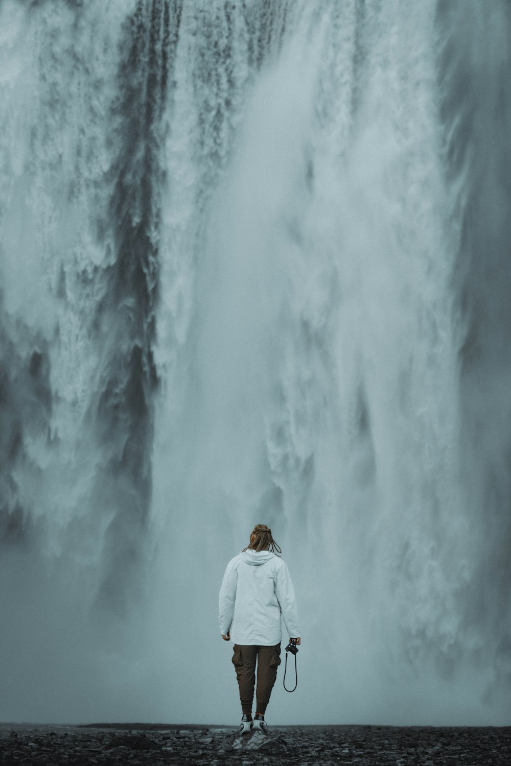 une personne debout devant une grande cascade