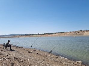 A sturdy camping chair with reinforced frame holding a fishing rod by a riverbank.