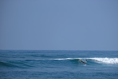 A surfer catching a gentle wave under a clear blue sky at a Moroccan beach.