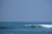 Smiling beginner surfer catching a small wave at Kedungu Beach under a clear blue sky.