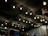 A ceiling covered with dark fabric is adorned with numerous string lights hanging from above. Below, a group of people can be seen standing and interacting in a dimly lit setting, likely an outdoor or semi-outdoor event.