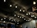 A ceiling covered with dark fabric is adorned with numerous string lights hanging from above. Below, a group of people can be seen standing and interacting in a dimly lit setting, likely an outdoor or semi-outdoor event.