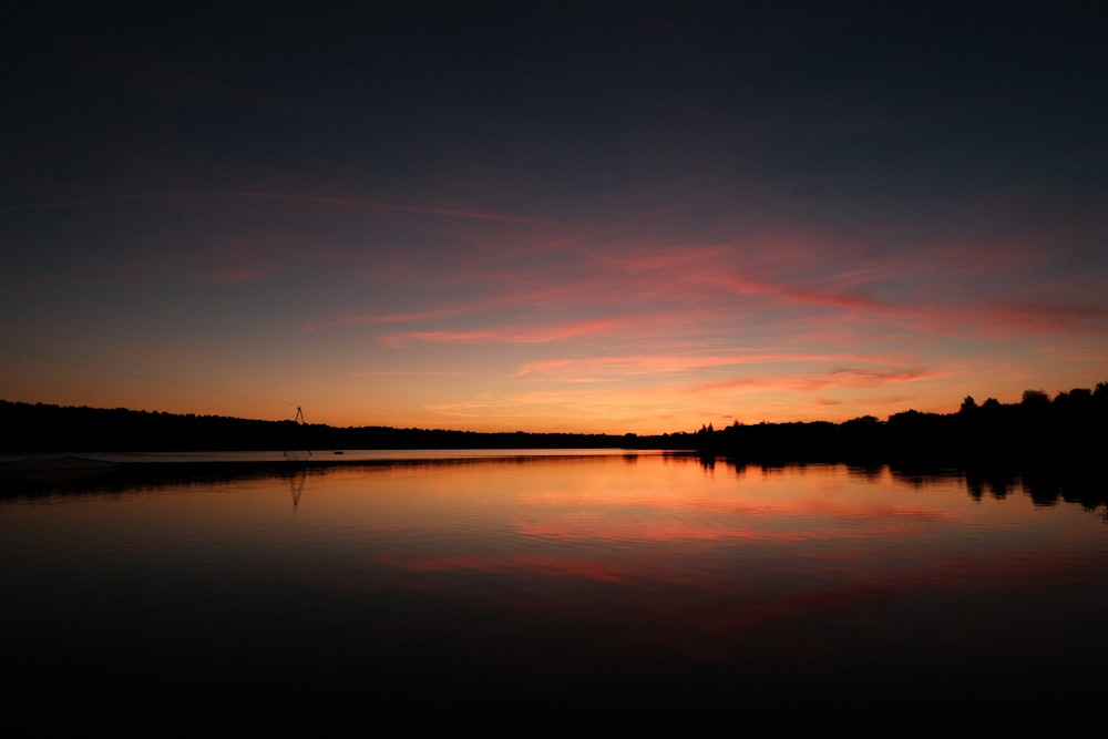 the sun is setting over a lake with trees in the background