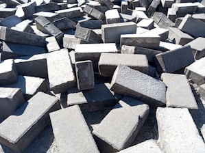 A large pile of rectangular concrete blocks scattered randomly on the ground, with sunlight casting shadows and highlighting the rough texture.