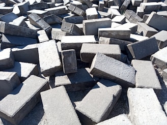 A large pile of rectangular concrete blocks scattered randomly on the ground, with sunlight casting shadows and highlighting the rough texture.
