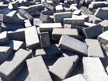 A large pile of rectangular concrete blocks scattered randomly on the ground, with sunlight casting shadows and highlighting the rough texture.