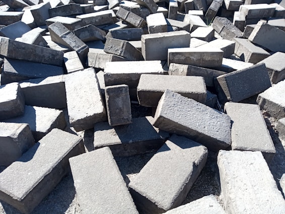 A large pile of rectangular concrete blocks scattered randomly on the ground, with sunlight casting shadows and highlighting the rough texture.