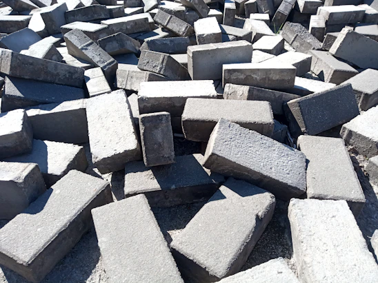 A close-up of mixed construction debris showing concrete chunks, bricks, and scattered metal pieces under sunlight.