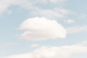 A serene sky with soft, fluffy clouds drifting across a light blue background.