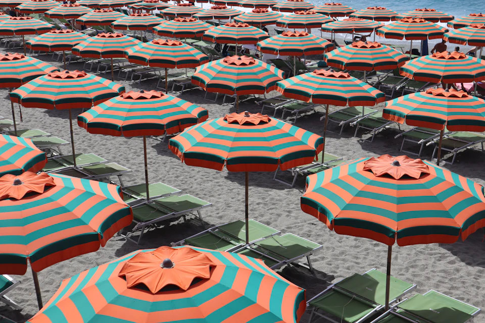 Rijen oranje-groen gestreepte parasols boven ligstoelen, op grijs zand